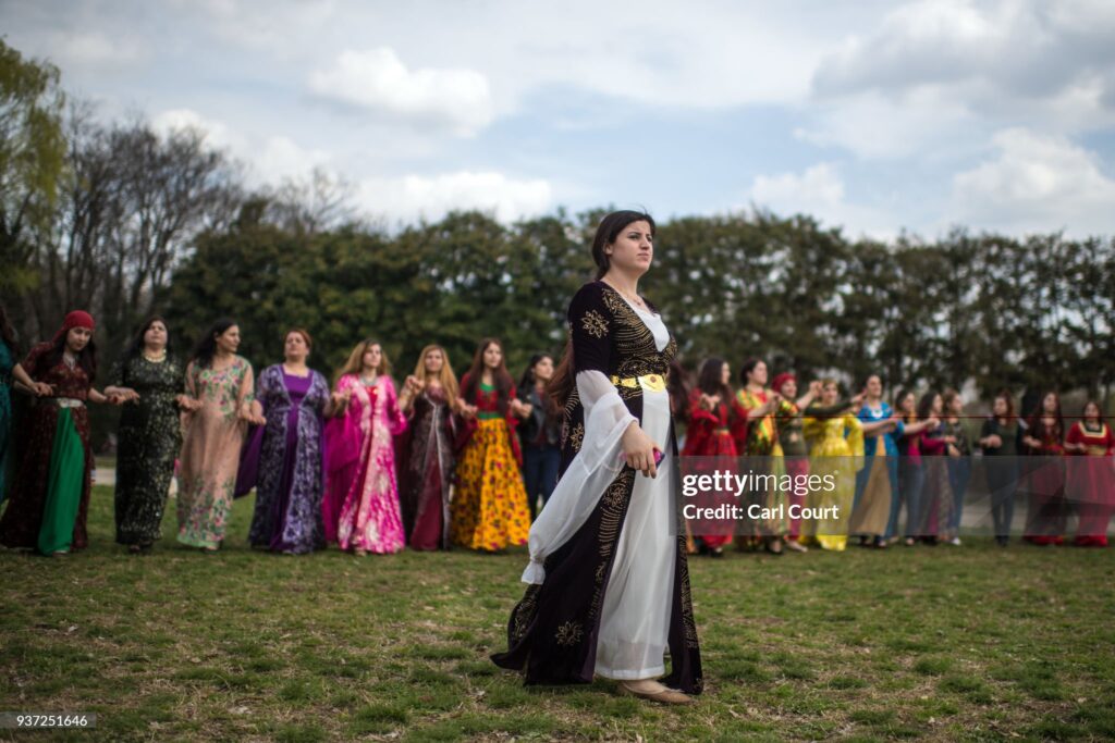 TOKYO, JAPAN - MARCH 24:  A Kurdish woman in traditional dress walks past friends as they dance during Nowruz celebrations on March 24, 2018 in Tokyo, Japan. Nowruz meaning 'new day' and marking the first day of spring, is widely celebrated by Kurdish communities around the world including in Japan where an estimated 2000 Kurds reside, many of whom are claiming refugeeæstatus owing to alleged human rights abuses in Turkey and Iraq. Although the Japanese government has issued some temporary permits allowing many to stay for years, no Turkish Kurd has ever been received refugee status in Japan, which would allow them to settle permanently.  (Photo by Carl Court/Getty Images)